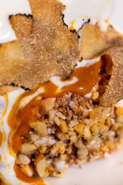 Karamelli ve fındıklı yatakta mantar dilimli dondurma. Sıvı karamel üzerine dökülür. Dondurma hafif, yuvarlak, geniş kenarlı seramik bir tabakta duruyor. Tabak hafif bir masa örtüsünün üzerinde. Yakınlarda bir yedek var.