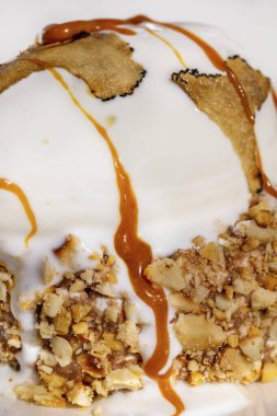 Karamelli ve fındıklı yatakta mantar dilimli dondurma. Sıvı karamel üzerine dökülür. Dondurma hafif, yuvarlak, geniş kenarlı seramik bir tabakta duruyor. Tabak hafif bir masa örtüsünün üzerinde. Yakınlarda bir yedek var.