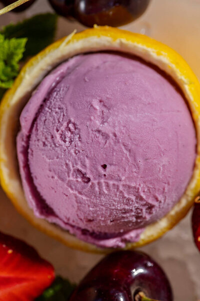 On a round, white plate are 6 balls of different types of ice cream and ice cream in chocolate on a stick. Ice cream lies on a small ice crumb, berries lie nearby. The plate is on a white tablecloth.