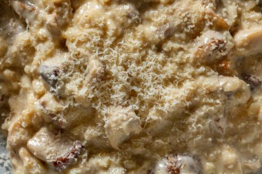 Italian dish of risotto with porcini mushrooms, creamy sauce and parmesan cheese. Risotto lies in a round, deep, ceramic plate. The plate is on a light wooden table. Nearby is a bottle of red wine and a wine glass filled with red wine.