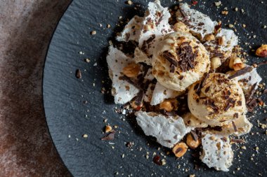 Çikolata parçalı dondurma topları, fındıklar, fıstıklar ve kremalar ahşap bir masada.
