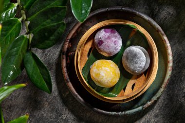 Vanilyalı dondurmalı yumuşak pirinç hamurundan yapılan Japon tatlısı, Mochi. Mango, yabanmersini ve yeşil çayla tatlandırılmış üç farklı Mochi. Mochi, altında bambu yaprakları olan bir sepetin içinde. Tatlı dolu bir sepet yuvarlaktır., 