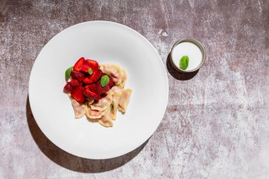 Çilekli hamur tatlısı ve gri arka planda bir tabakta nane şekeri ve kasede ekşi krema.