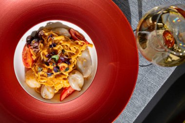 Spaghetti with squid, octopus, sprouts, tomatoes, cheese and sauce in a plate on the table with a glass of wine, a bottle of wine, pepper and salt