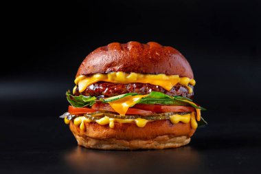 Hamburger, pirzola, peynir, kabak, salata, sos, domates ve siyah arka planda salatalık turşusu.