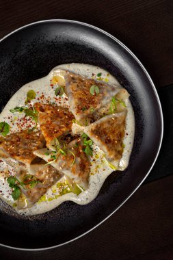 Triangular dumplings with sesame seeds, sprouts, white and brown sauce, basil and nasturtium leaves in a plate on the black table