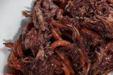 Italian dish. Pasta Bucatini with finely chopped duck fillet in plum sauce. The pasta lies in a deep, round, wide-brimmed ceramic plate. The plate is on the table on a white tablecloth. Next to the plate is a long-stemmed glass with red wine, a bowl 