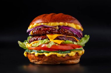 Çift pirzolalı hamburger, soğan, peynir, marul, sarı sos, domates ve salatalıklı siyah arka plan 