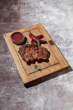 Kızarmış domuz eti, kırmızı sos, kırmızı biber, ahşap tahtada tuz ve fesleğen ve gri arka plan.