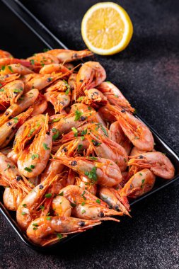 Limonlu ve maydanozlu haşlanmış karidesler koyu mavi bir zemin üzerinde demir bir fırın örtüsünün üzerinde yatıyor.