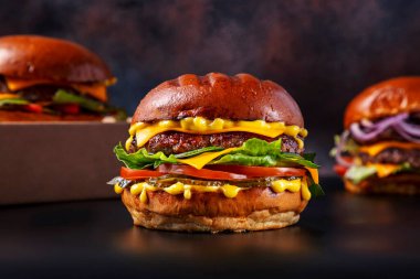 Hamburger ile pirzola, peynir, kabak, salata, sos, domates ve salatalık turşusu siyah arka planda duman, karton kutu ve diğer hamburgerler