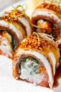 Pan-Asya mutfağı, unagi soslu yılan balığı, pirinç, salatalık ve Philadelphia peyniri. Susam tohumları ve mikroyeşil lahanalarla kaplı. Suşi yuvarlak, hafif, düşük kenarlı seramik bir tabakta yatar. Yakında zencefil turşusu ve wasabi küpü var. Tabak Stan.