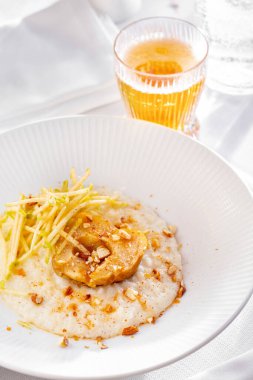 Porridge with sweet potatoes, apple and hazelnuts in a plate on a white table with a glass of juice