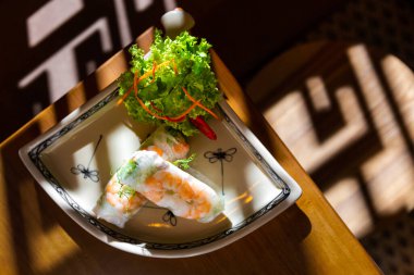 Pirinç kağıdında karides, peynir, sos, lahana, biber ve friz salatasıyla birlikte masanın kenarında restoranla çevrili bir tabakta yuvarlan.