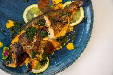 Fried fish with lemon, sauce and green petals in a plate that stands on the table