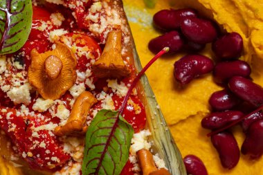 Mercimek püresi, iki yarım fırında patlıcan, domates, paprika ve parmesan peyniri, üstünde chanterelle gibs ve üstünde marul yaprakları. Kaynamış kırmızı fasulye püre üzerinde uzanıyor. Yiyecek mavi, yuvarlak, seramik bir tabakta yatıyor. Tabak duruyor.