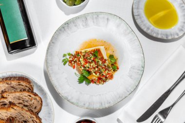 Italian dish. Sea bass fillet fried in a grill pan with vegetable tabouleh. The food lies in a light handmade ceramic plate. Nearby is a bowl of olives, a saucer of olive oil, a plate of buckwheat bread and grissini, and a dark bottle of olive oil wi