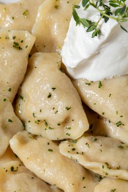 Ukrayna yemeği, ördekli börek. Yemek yuvarlak, beyaz, derin, seramik bir tabakta yatıyor. Üstünde ekşi krema ve kekik var. Üzerine ince doğranmış dereotu serpilmiş. Tabak koyu renk, kumaş arka plan, kahve rengi..