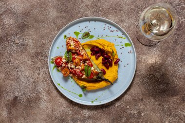 Mercimek püresi, iki yarım fırında patlıcan, domates, paprika ve parmesan peyniri, üstünde chanterelle gibs ve üstünde marul yaprakları. Kaynamış kırmızı fasulye püre üzerinde uzanıyor. Yiyecek mavi, yuvarlak, seramik bir tabakta yatıyor. Tabak duruyor.