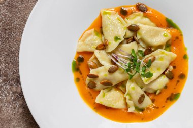 Porcini köftesi, kabak sosu, kabak çekirdeği, balzamik pesto sosu, mikroyeşil lahanalar. Yiyecek beyaz, yuvarlak, derin, seramik bir tabakta yatıyor. Tabak koyu renk, kumaş arka plan, kahve rengi..