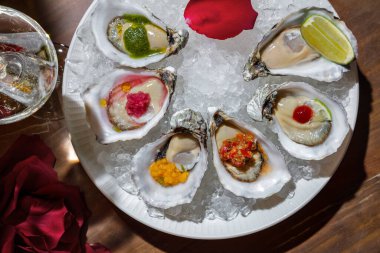 Oysters with sauces, lemon, flower petal in a plate with ice standing on the table with a glass of champagne