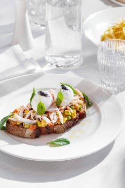 Sandwich with salmon, crab meat, boiled egg, avocado, basil and mung bean salad in a plate on a white table with a glass of water
