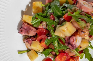 Seafood salad with scallop, octopus, wine vinegar, asparagus, potatoes and tomatoes. The salad lies in a light ceramic plate, next to it is a glass of rose wine. Food and wine are on a table with a light tablecloth.