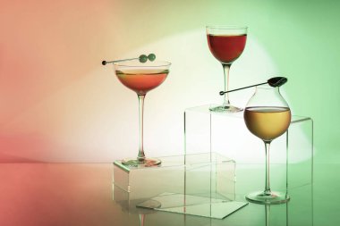 Three cocktails are poured into high-stemmed glass goblets. Two red cocktails, one yellow. Cocktails stand on plastic coasters, coasters stand on a glass, transparent background. The glass lies on a paper background with a color gradient of red, yell