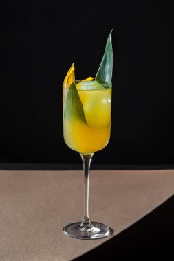 Malibu and Pineapple rum-based cocktail. The composition includes white rum, pineapple juice, mango liqueur. On top of the liquid is a round ball of ice. The cocktail is poured into a patterned crystal champagne glass on a high stem, with a bamboo le