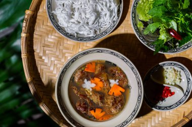 Birinci kasede erişte, ikinci kasede havuç, et ve turpla çorba, frizse salatası, maydanoz, fesleğen ve marul üçüncü kasede, ve kırmızı biber ve dördüncü kasede doğranmış sarımsak. Tüm tabaklar arka planda yuvarlak bir masada.