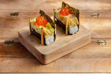 Unwrapped roll with nori, rice, salmon, tobiko caviar, sauce and salmon caviar on a wooden stand on a wooden table