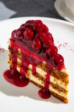 Slice of cake with cherries and cherry jam in a plate on the table