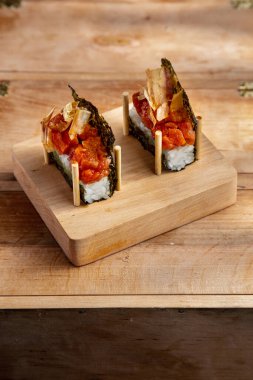 Unwrapped roll with nori, rice, fish pieces and onions on a wooden stand on a wooden table