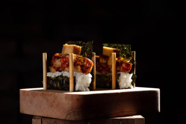 Unpackaged roll with nori, rice, fish meat and tofu on a wooden stand on a black background