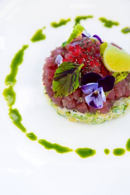 Salad with tuna, lemon, sorrel, violet, sesame, tobiko caviar, sauce, avocado, cucumber and mayonnaise on a plate who is standing on the table