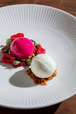 Ahududu aromalı şerbet ve ahududulu dondurma, nane, böğürtlen ve kızılcık ile ahşap bir masada.