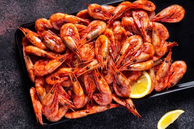 Limonlu ve maydanozlu haşlanmış karidesler koyu mavi bir zemin üzerinde demir bir kabın üzerinde yatıyor.