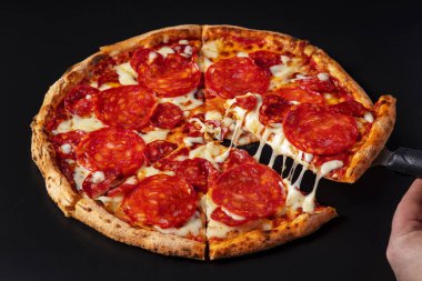 Sucuklu pizza, sosis, peynir ve ketçaplı siyah arka plan. Elinde spatulada pizza tutan bir adam.