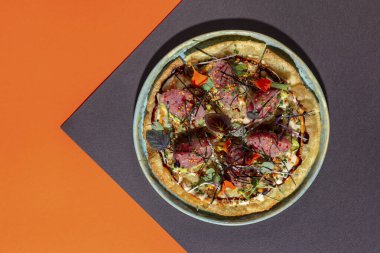 Japon pizzası veya yassı ekmek, okonomiyaki, roti, ton balığı tartarı, taze avokado, mikroyeşil lahanalar, susam tohumu, mango sosu, marul, ince pirinç hamuru. Roti hafif, yuvarlak, düşük kenarlı seramik bir tabakta yatıyor. Tabak kağıdın üzerinde, siyah...