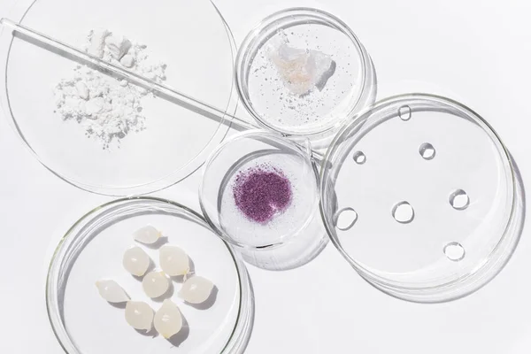 Glass, transparent, medical flasks, different sizes, for laboratories and a glass rod, lie on a white background. The flasks contain pickled onions, purple captcha powder, powdered sugar and drops of gin.