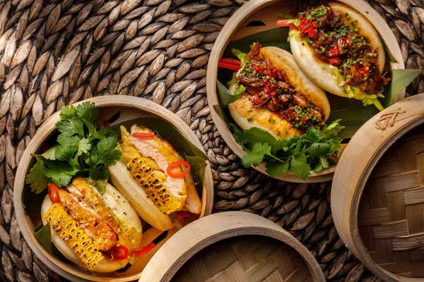 Buns with onions, fish meat, parsley, pepper and sauce in a basket that stands on a wicker table with another basket in which buns with corn, sesame seeds, fish meat, sauce, parsley and chili
