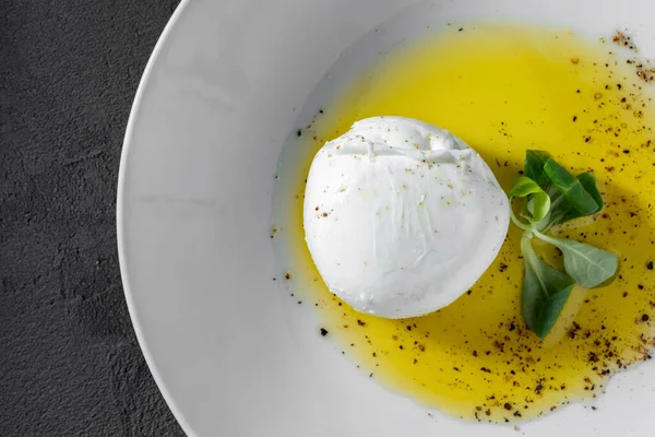 意大利莫扎瑞拉 撒满了香草 躺在一个白色的陶瓷盘上 橄榄油洒在盘子上 附近是一片生菜叶子 盘子位于灰色的石质背景上 — 图库照片