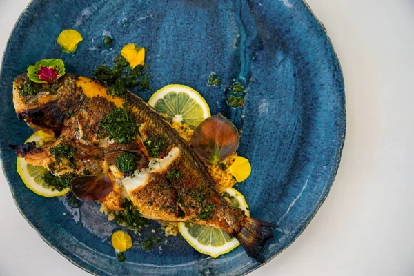 Fried fish with lemon, sauce and green petals in a plate that stands on the table