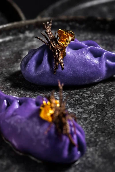 Purple dumplings with truffle stripes and gold leaf in a black plate