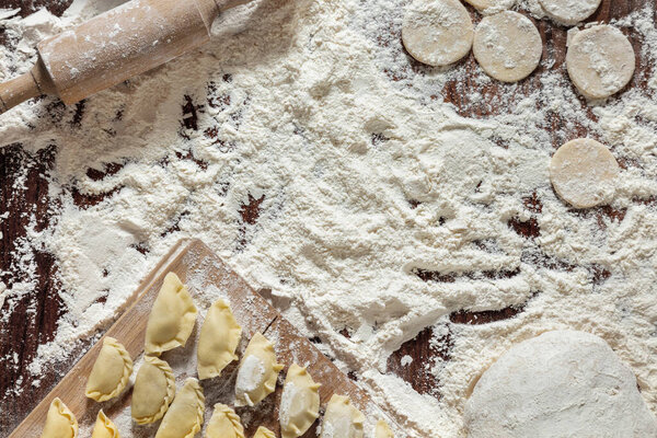 The process of making dumplings. The woman is dressed in a white, traditional Ukrainian vyshyvanka and a brown skirt. She makes dumplings on the table with her hands. Wraps mashed potatoes in round dough pieces. The table is covered with flour. Nearb