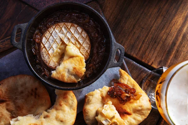 Fried brie cheese with fried onions in a frying pan on the table with Georgian bread and a glass of beer