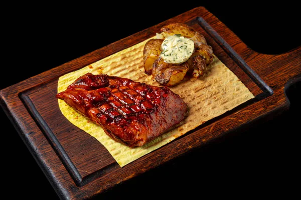 Grilled grilled steak with sauce, potatoes, butter, parsley and pita bread on a wooden board on a black background