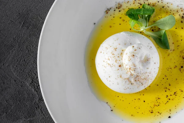 意大利莫扎瑞拉 撒满了香草 躺在一个白色的陶瓷盘上 橄榄油洒在盘子上 附近是一片生菜叶子 盘子位于灰色的石质背景上 — 图库照片