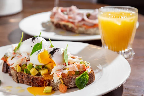Karidesli sandviç, haşlanmış yumurta, avokado, fesleğen ve mung fasulyesi salatası masada bir tabak daha ve bir bardak meyve suyu.