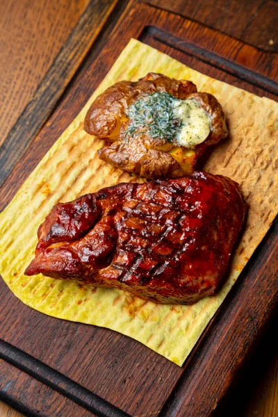 Grilled steak with sauce, potatoes, butter, parsley and pita bread on a wooden board standing on the table